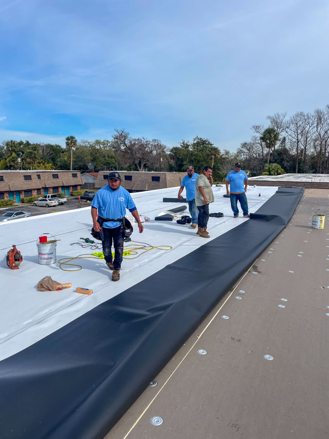 Roofer meticulously installing a new commercial roofing layer, focusing on precision and safety measures.