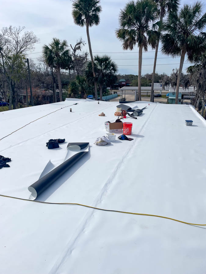 Roofer standing on a newly finished commercial flat roof, showcasing a completed roofing project with tools around, under a clear sky.