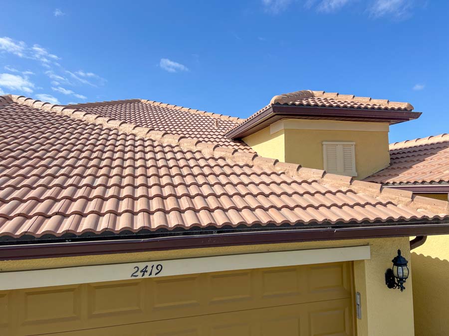 A roofer carefully replaces tiles on a clay tile roof with a scenic waterfront backdrop, demonstrating precision in high-altitude roofing work.