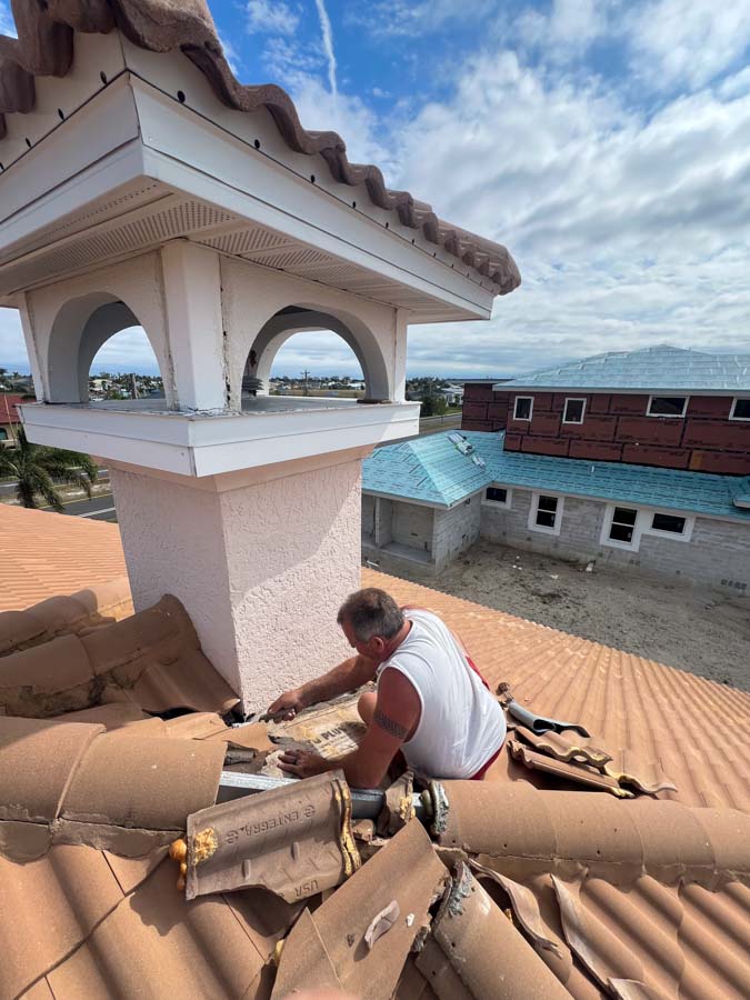 A roofer repairs damaged clay tiles on a residential roof, showcasing detailed work and roof maintenance under a clear sky.
