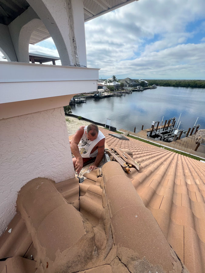 Dynamic view of a roofer adjusting tiles on a steep clay tile roof against a blue sky, highlighting the challenges of roofing work.